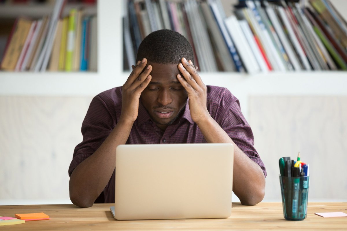 A person holding his head in his hands while looking disappointed at his laptop.