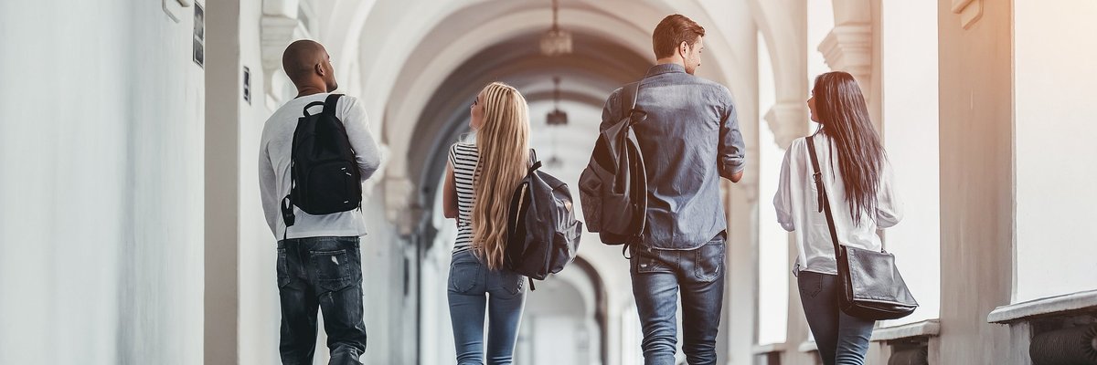Four students walking through an arched school hallway.