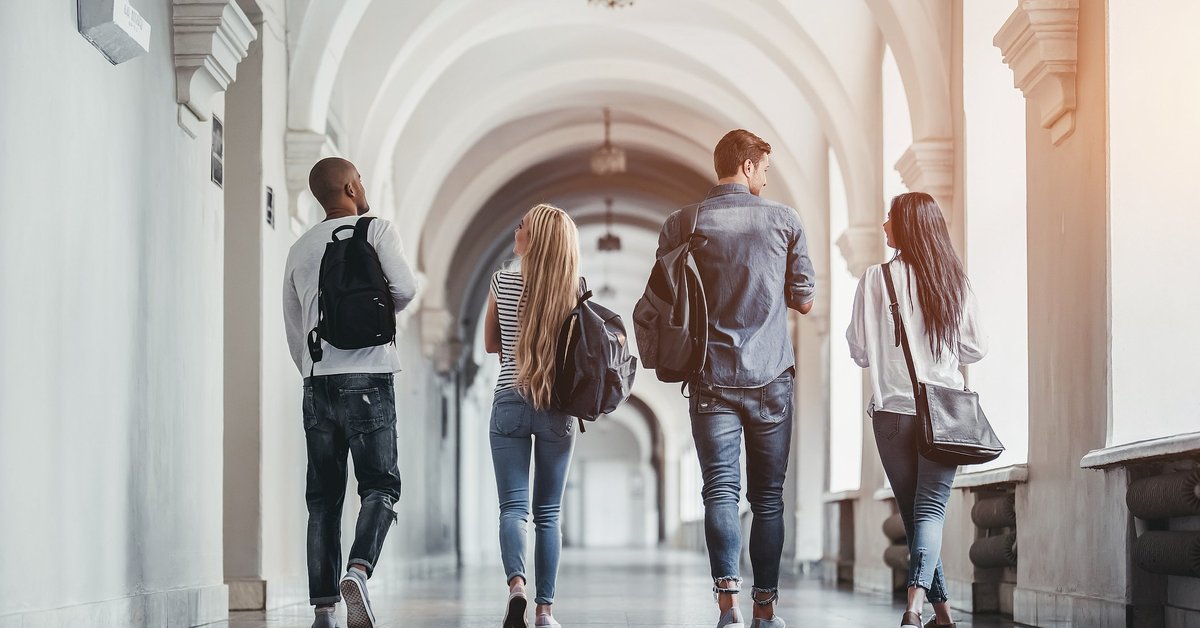 Four students walking through an arched school hallway.