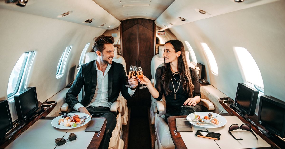 Successful couple making a toast with champagne glasses while having canapes aboard a private airplane