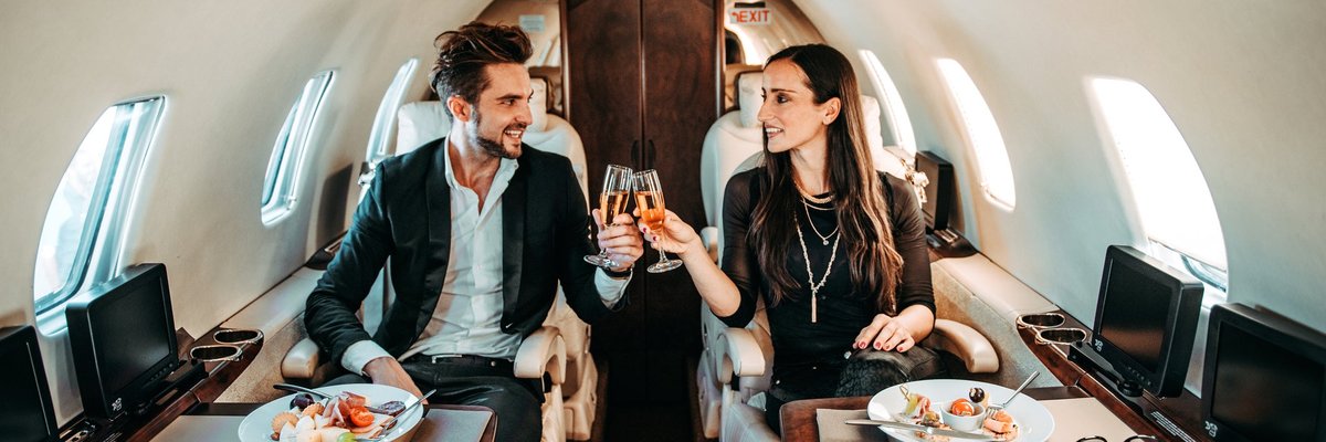 Successful couple making a toast with champagne glasses while having canapes aboard a private airplane