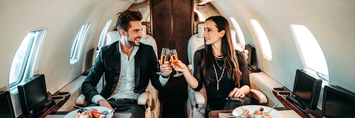 Successful couple making a toast with champagne glasses while having canapes aboard a private airplane