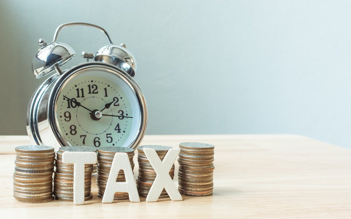 A pile of coins spelling out "Tax" stands in front of a clock.