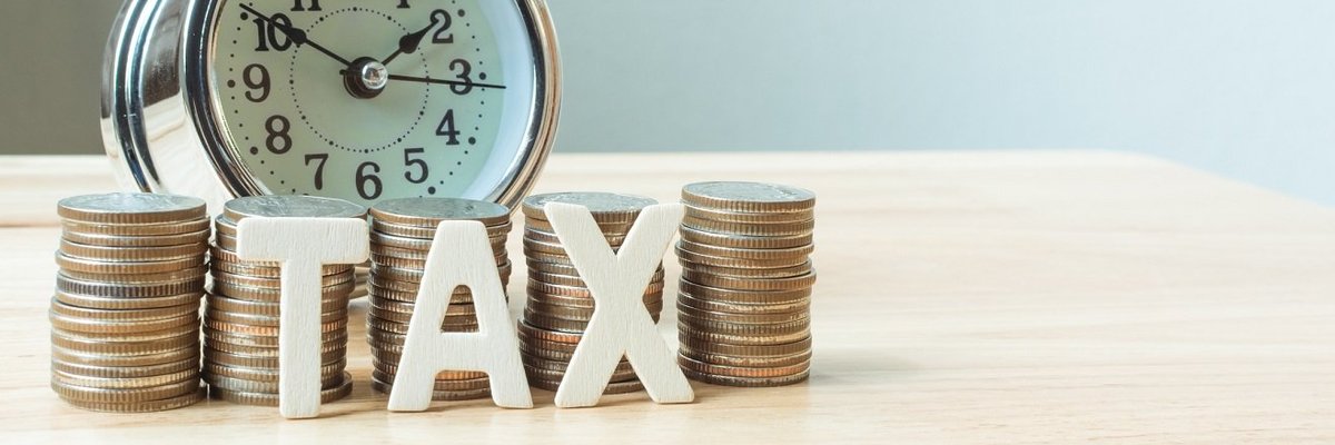 A pile of coins spelling out "Tax" stands in front of a clock.