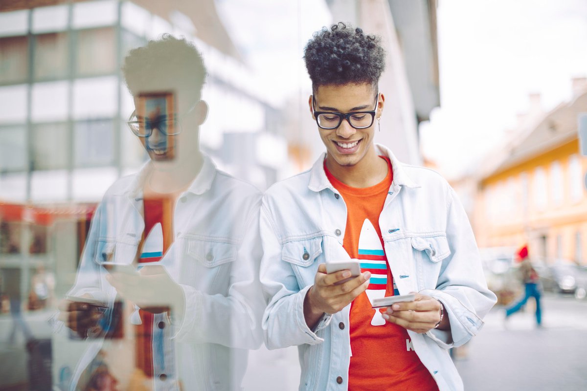 Teen boy using his phone and holding a credit card in the city.