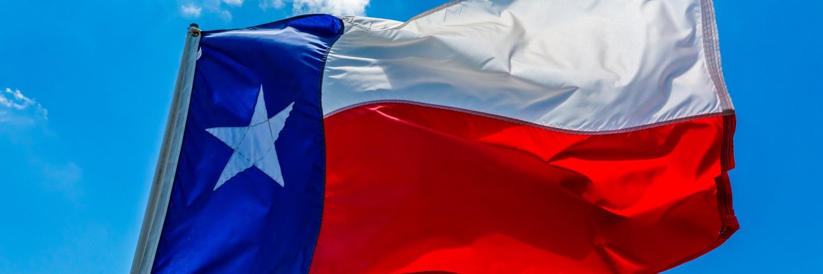 The state flag of Texas flying in front of a bright blue sky.