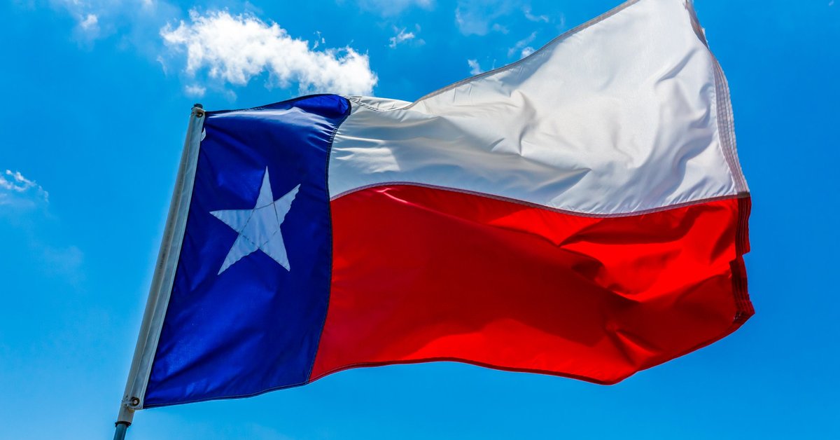 The state flag of Texas flying in front of a bright blue sky.