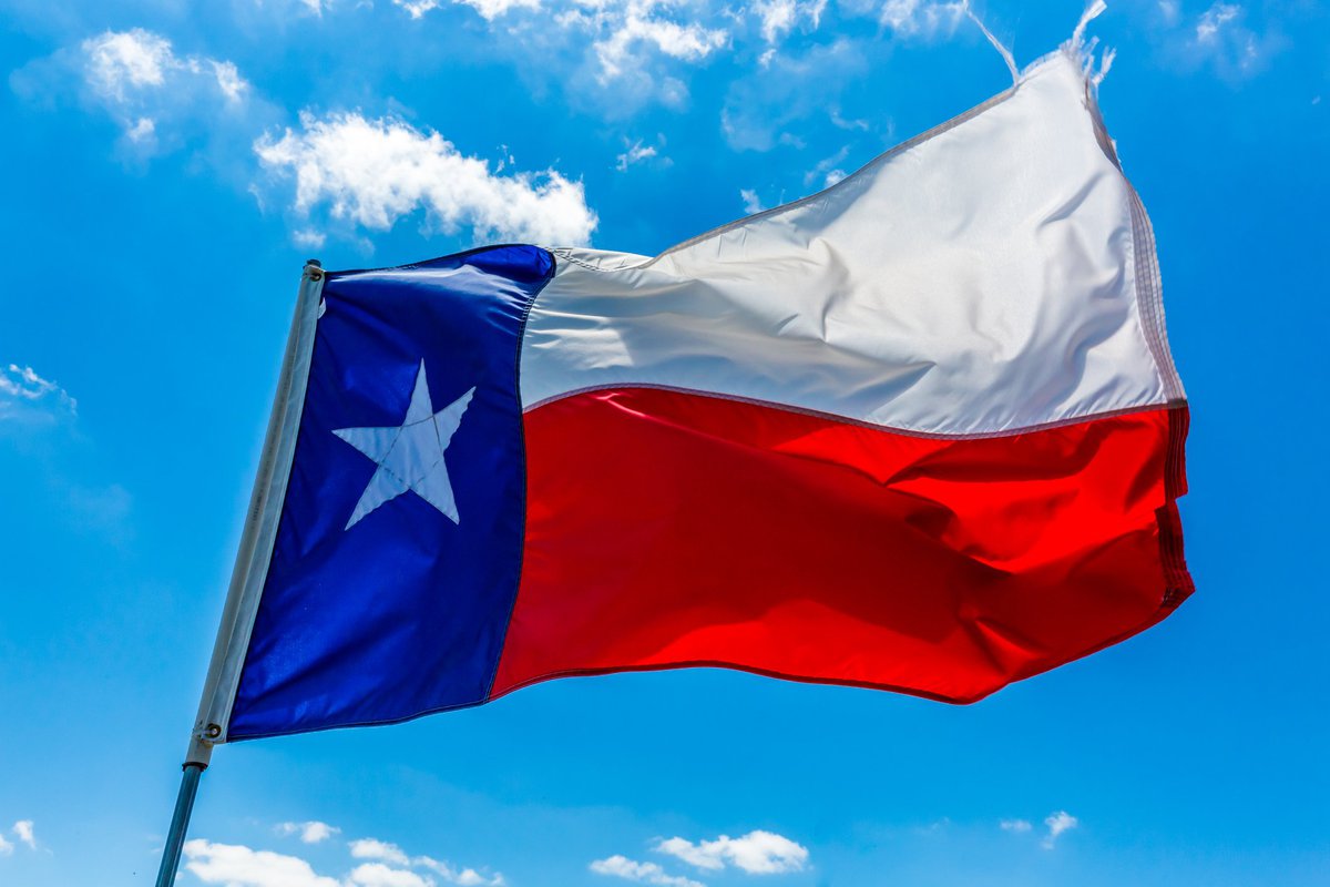 The state flag of Texas flying in front of a bright blue sky.