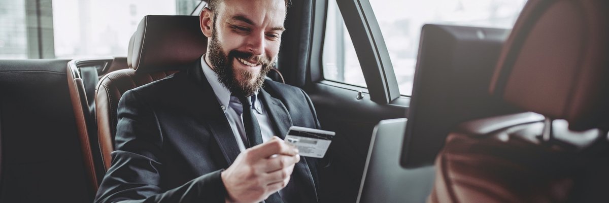 Man in suit in the back of a luxury car with laptop in his lap holding a credit card.
