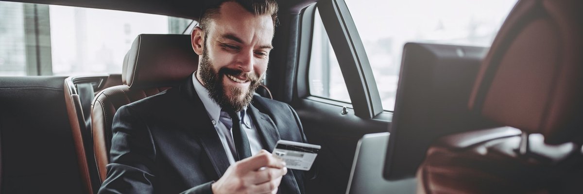 Man in suit in the back of a luxury car with laptop in his lap holding a credit card.