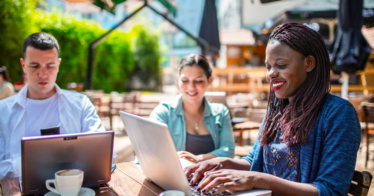 Three adults sitting on a patio utilizing their laptops.