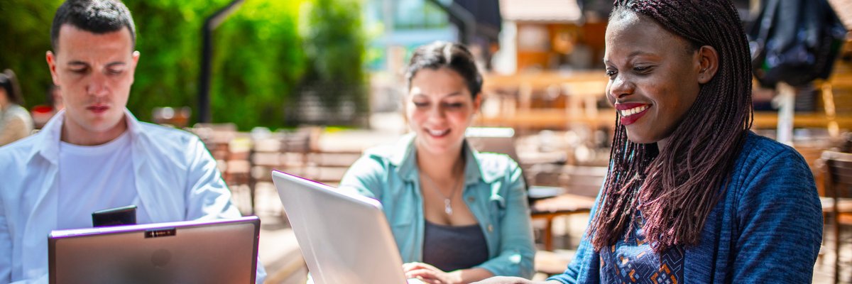 Three adults sitting on a patio utilizing their laptops.