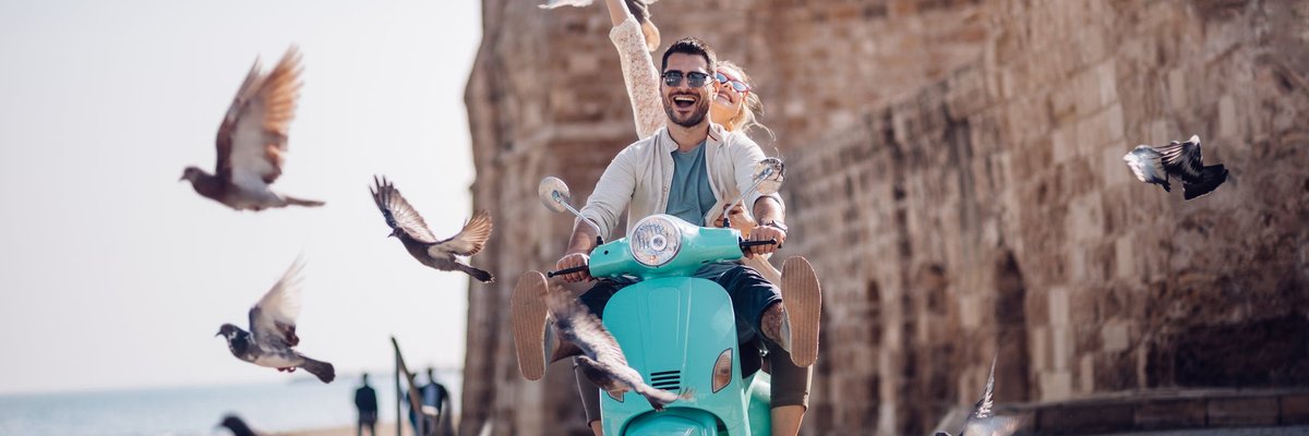 Tourists riding a motorized scooter through an old European town.