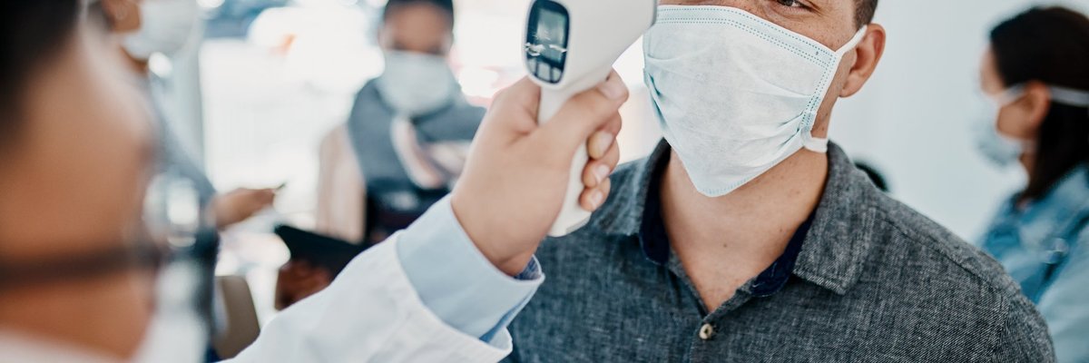 Traveler in face mask getting his temperature checked.
