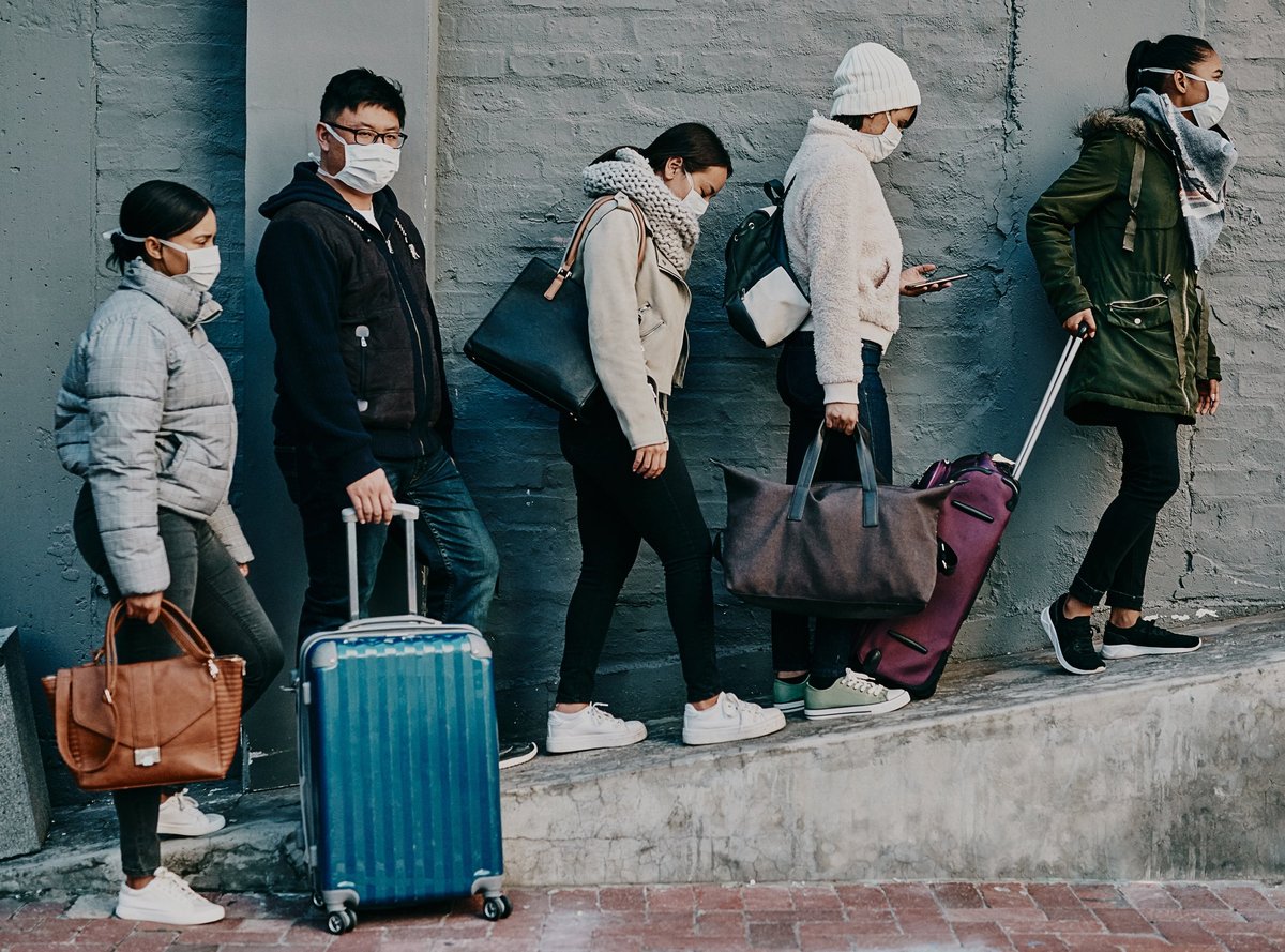 Travelers with masks and luggage during the pandemic.