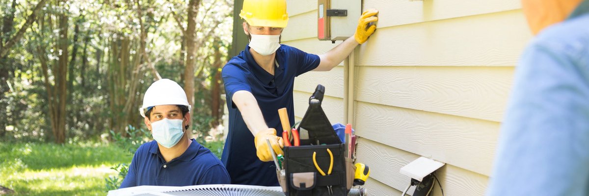Two air conditioner workers service outside unit.
