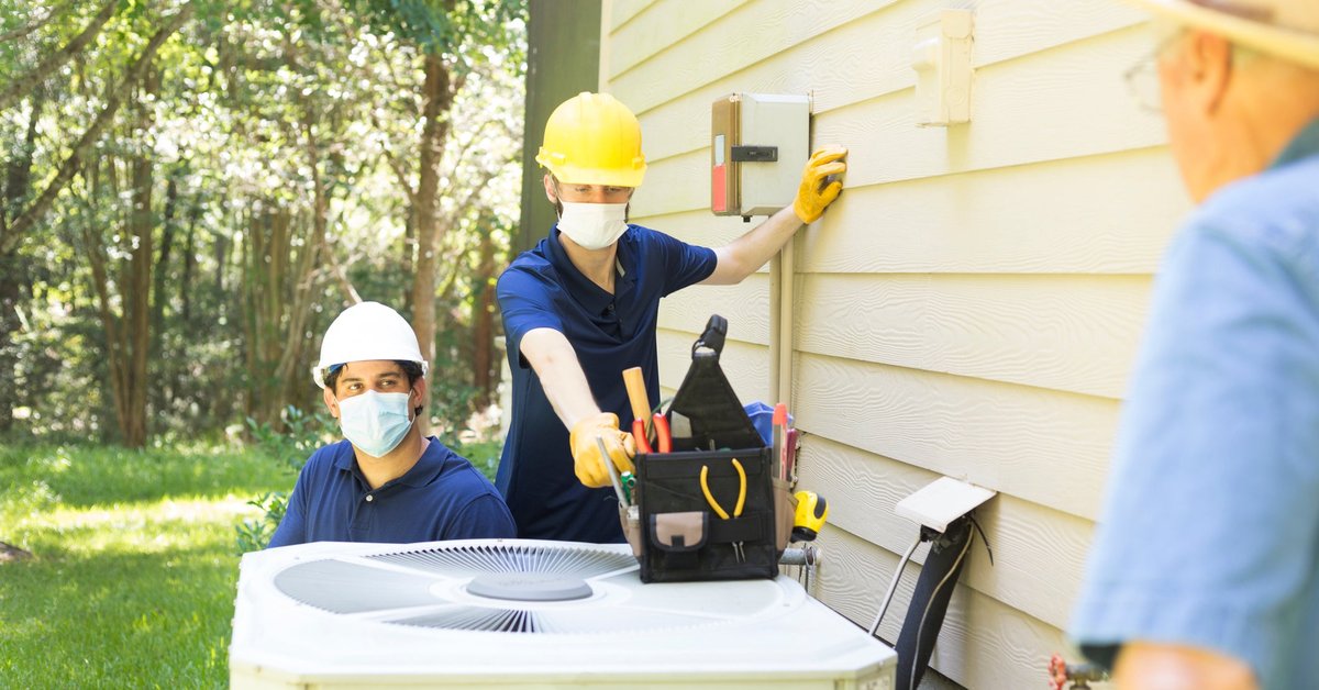 Two air conditioner workers service outside unit.