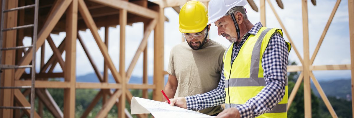 Two builders review blueprints inside an in-process new build home.