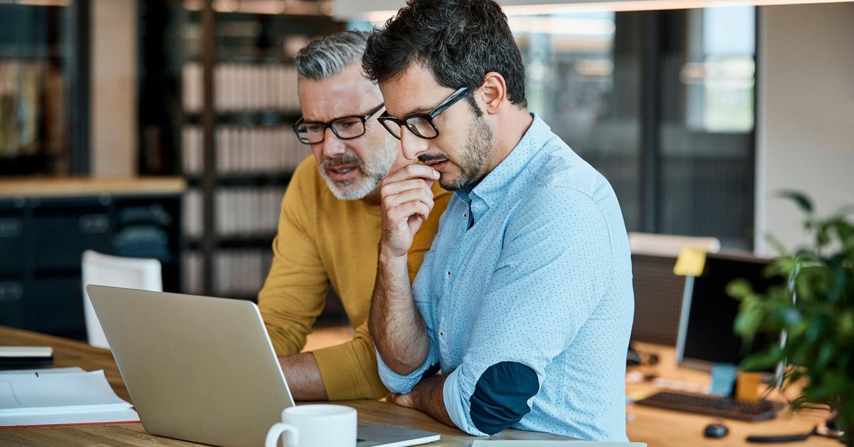 Two men in thought looking at a laptop screen together.