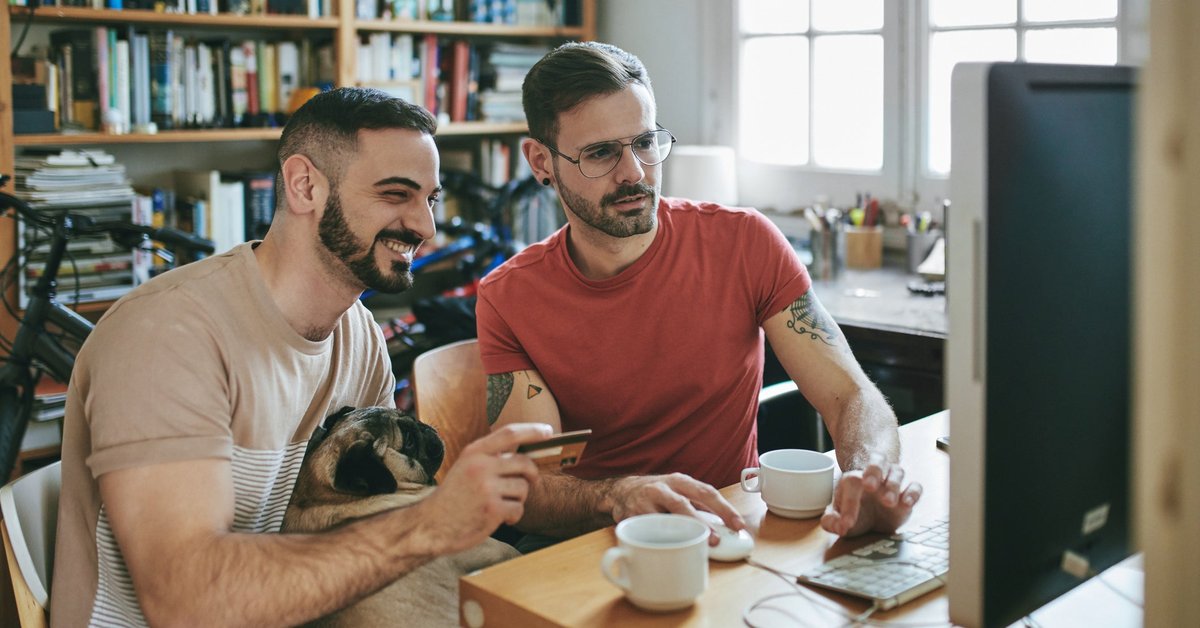 Two men smile as they look a computer. One is holding a credit card.