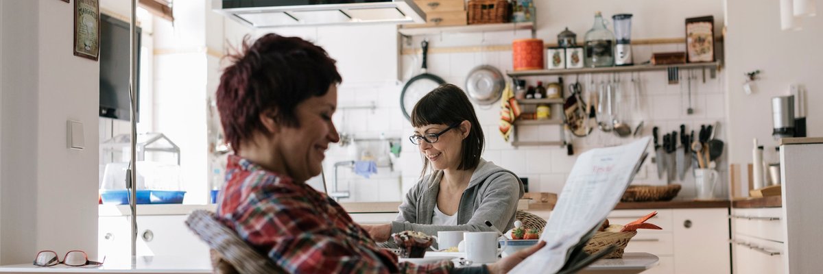 Two people in a kitchen reading the news.