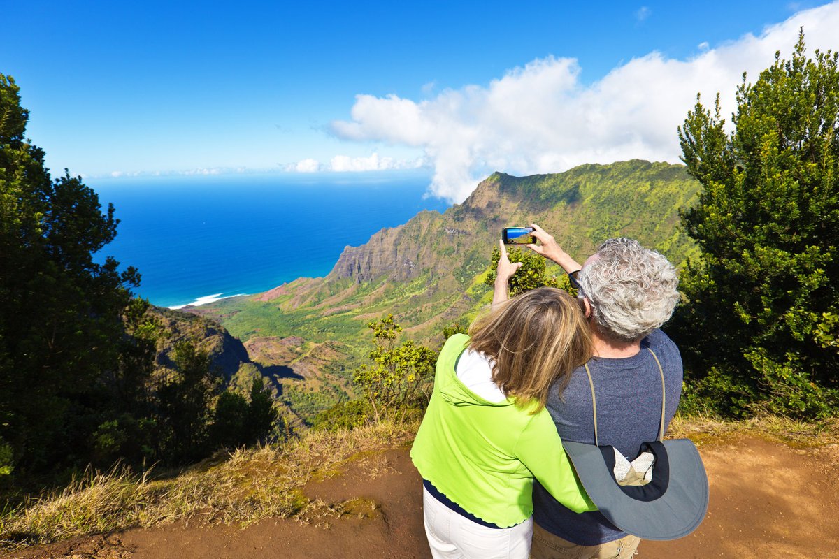 Two people taking photos at a scenic overlook featuring oceans and green hills