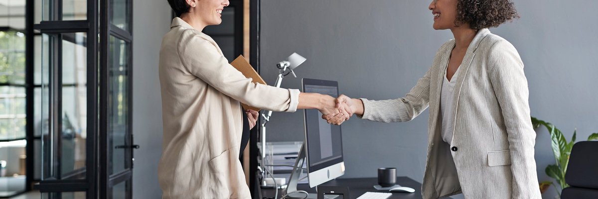 Two professionally dressed women shaking hands in an office