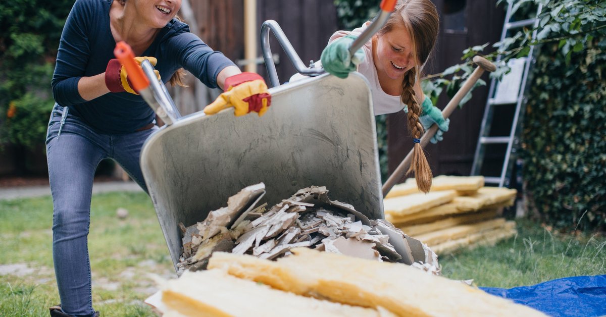 Two women dumping home renovation scraps in a pile outside