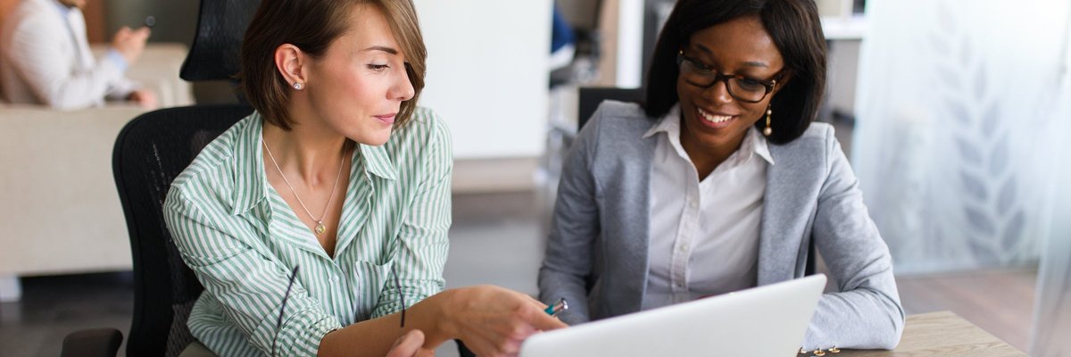 Two women looking at charts on tablet and laptop