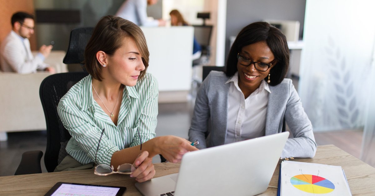 Two women looking at charts on tablet and laptop