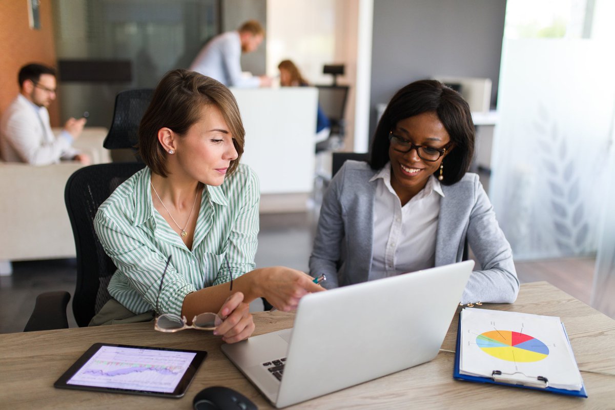 Two women looking at charts on tablet and laptop