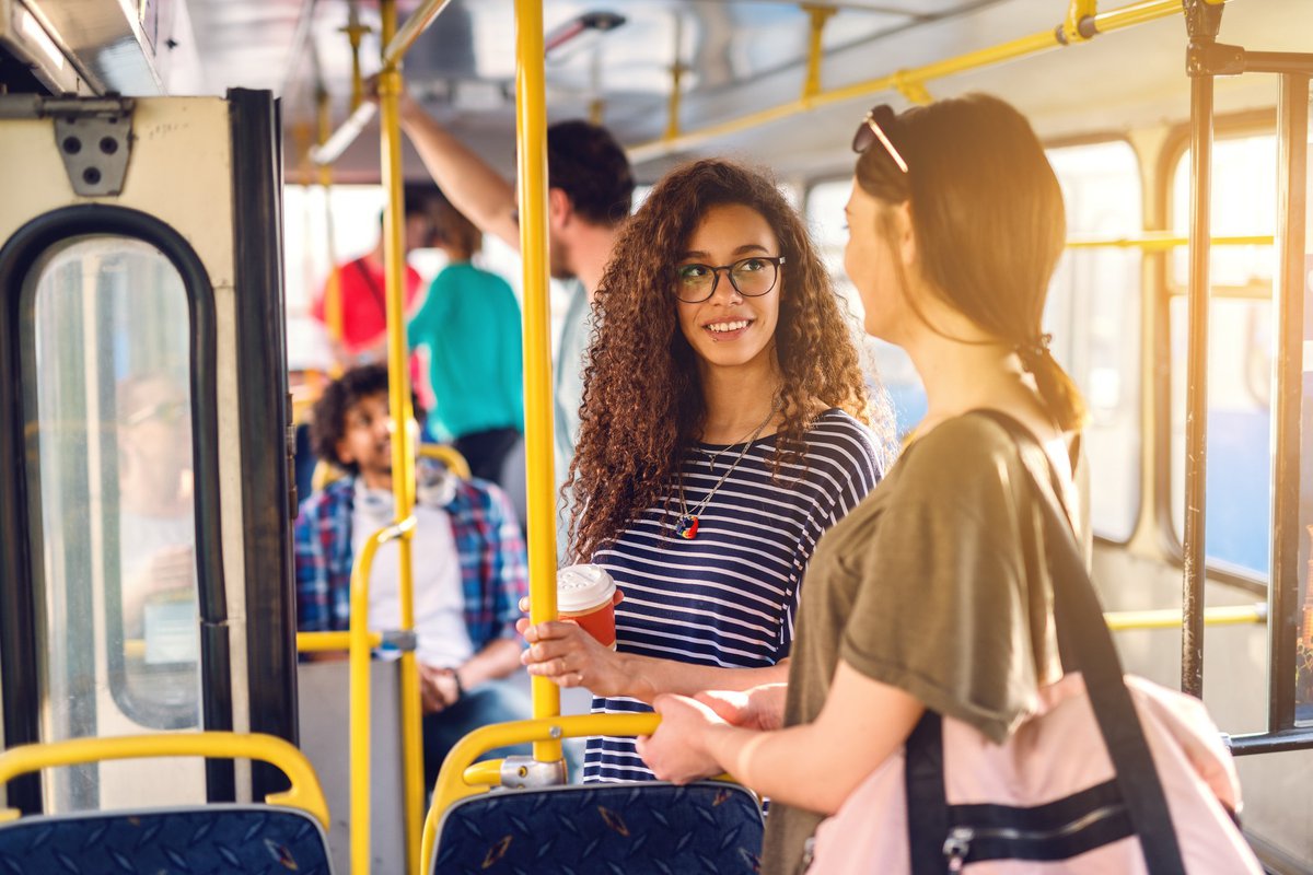 Two women chatting while standing on a sunny bus.