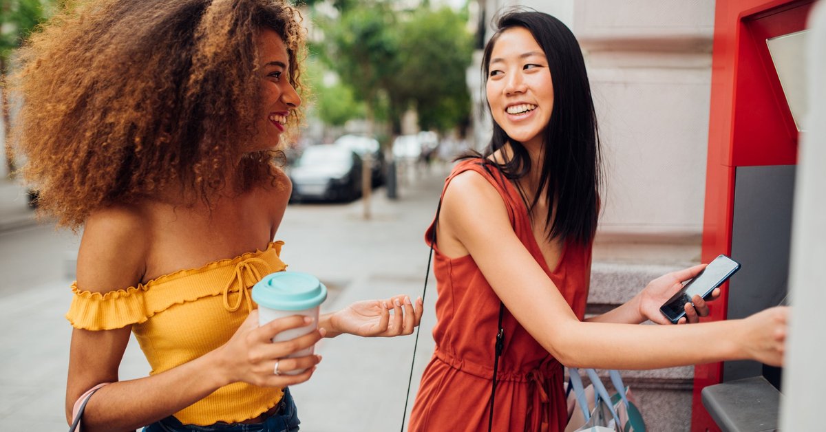 Two women smile as one uses her debit card at the ATM
