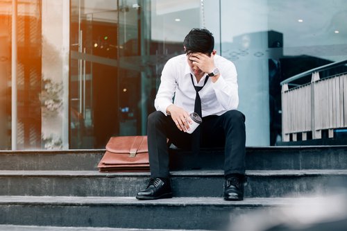 Man sitting on steps next to briefcase with head in his hands