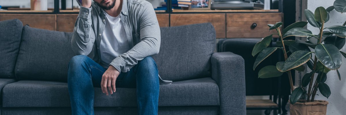 An upset man sitting on a couch with his hand on his head.
