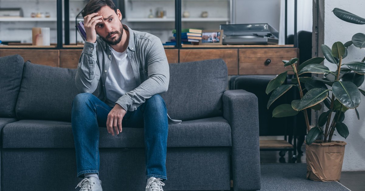 An upset man sitting on a couch with his hand on his head.