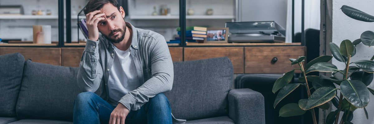 An upset man sitting on a couch with his hand on his head.