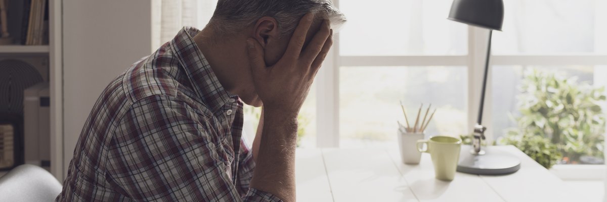 An upset man with his hands on his head on the phone at his desk.