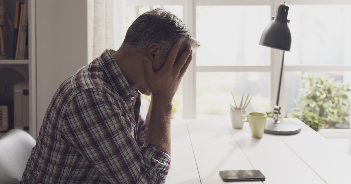 An upset man with his hands on his head on the phone at his desk.