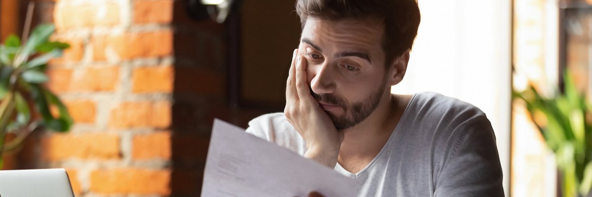 An upset man reading over his bills with his hand on his face.