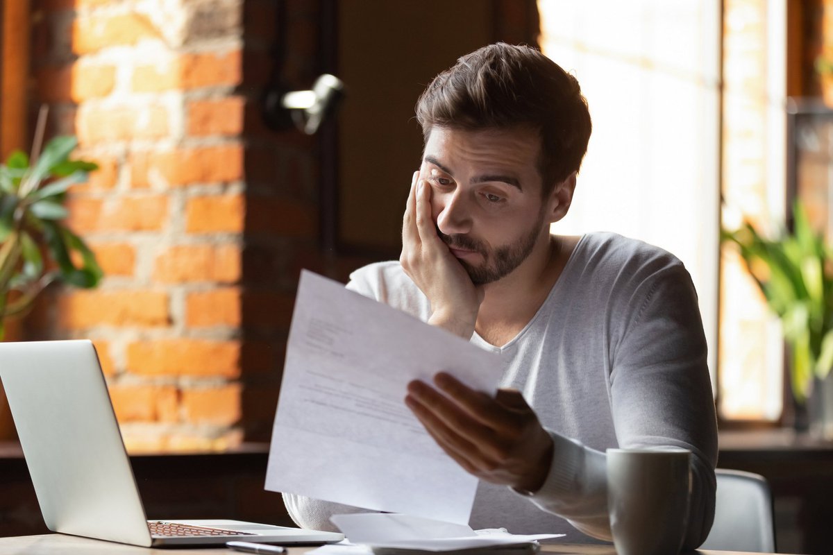 A distraught man sitting at his desk and reading bills with his chin in his hand.