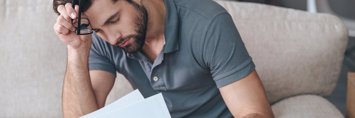 An upset man reading bills on his couch.