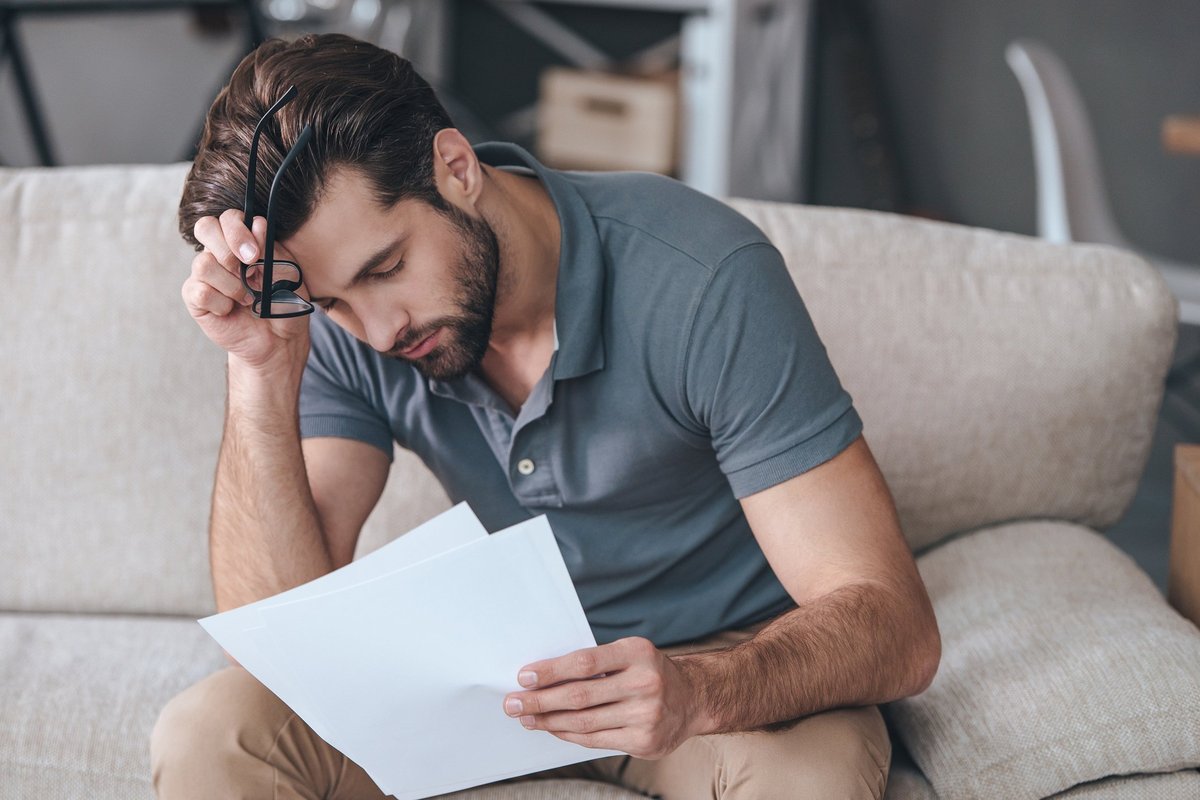 An upset man reading bills on his couch.