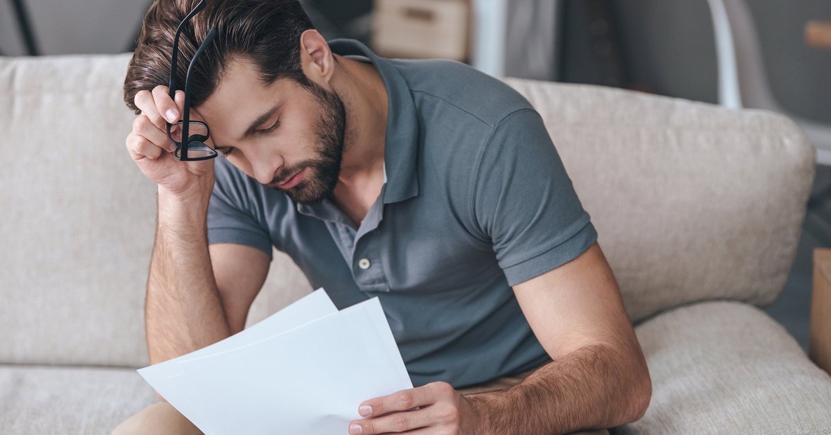An upset man reading bills on his couch.