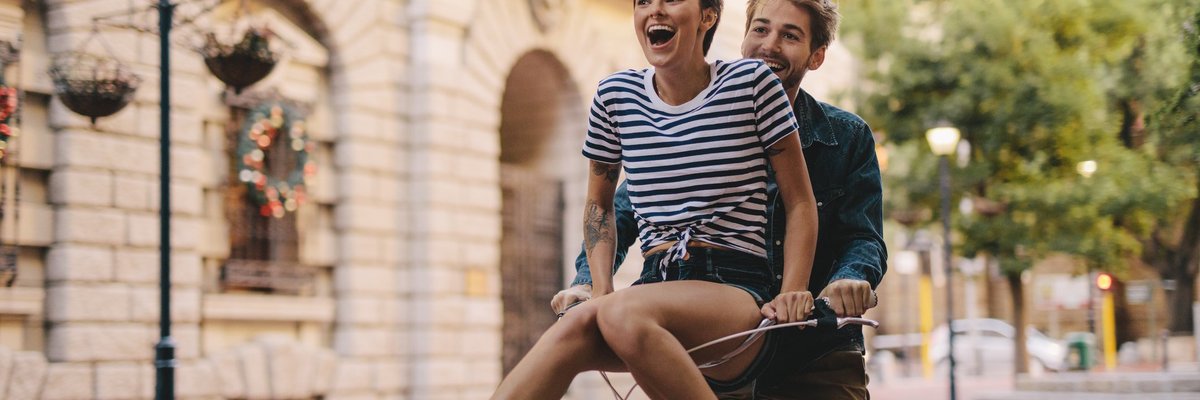 Young man riding a bike with a young woman laughing on the handlebars.