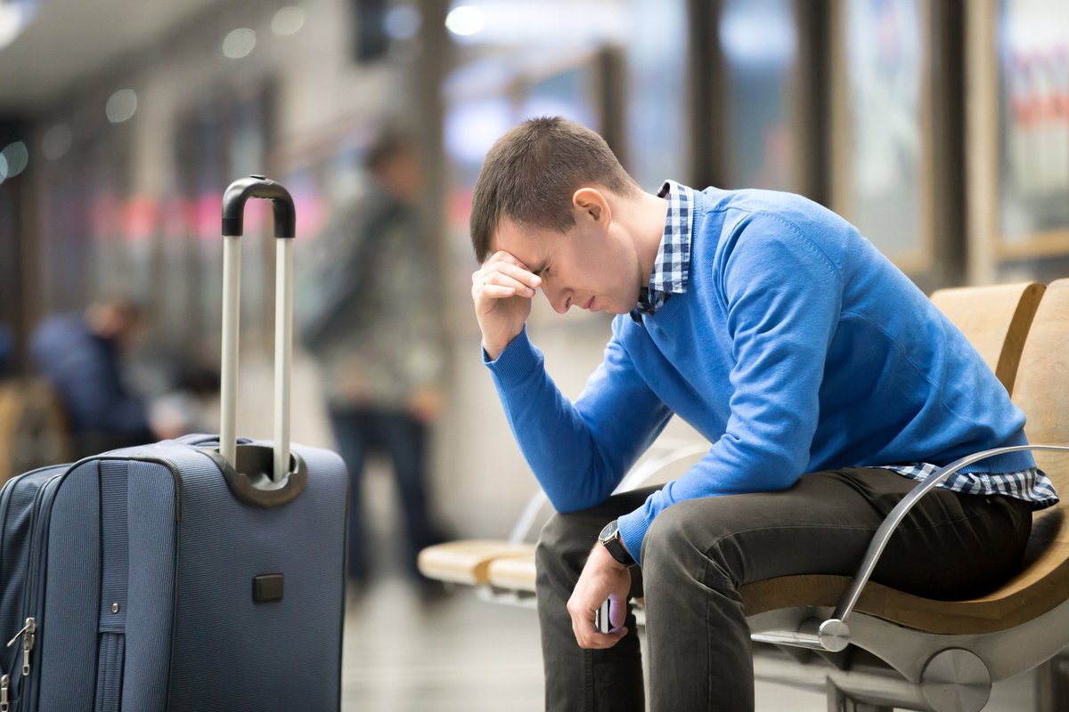 Dejected man sitting at airport beside his luggage,