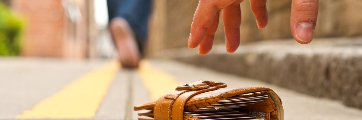 A person walking away from the wallet they dropped on the ground and a thief's hand hovering over it.