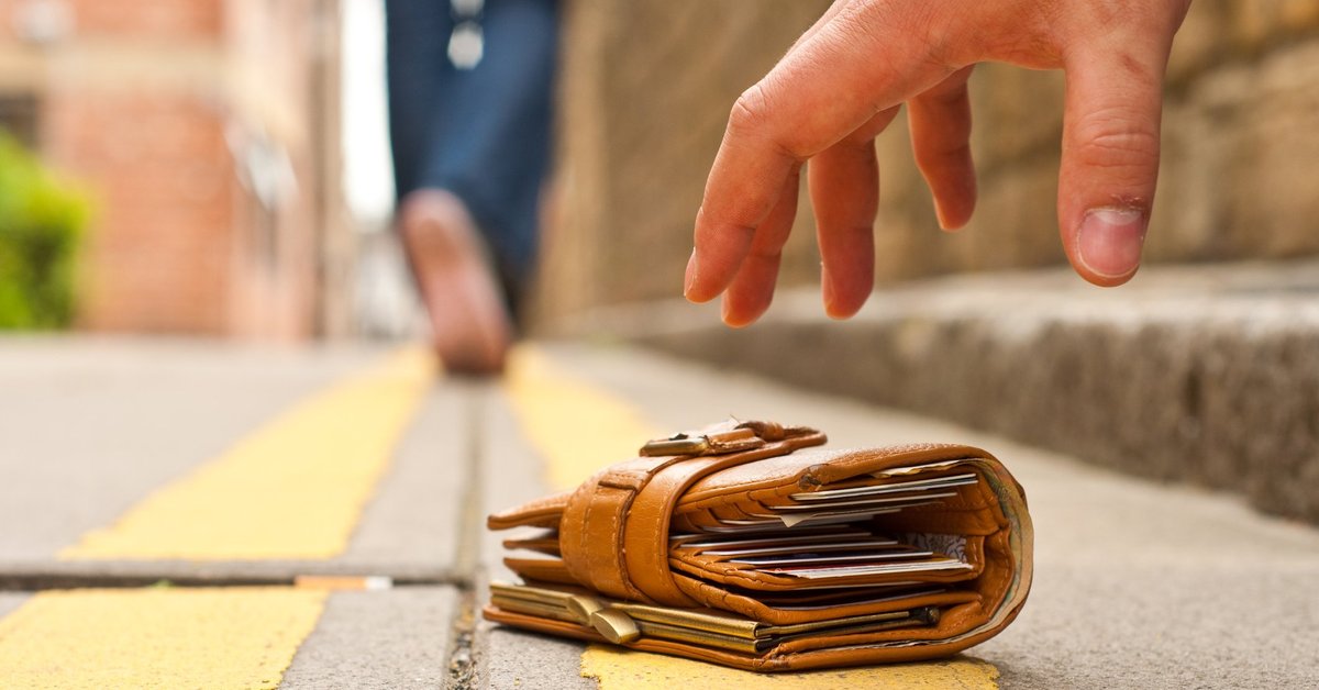 A person walking away from the wallet they dropped on the ground and a thief's hand hovering over it.