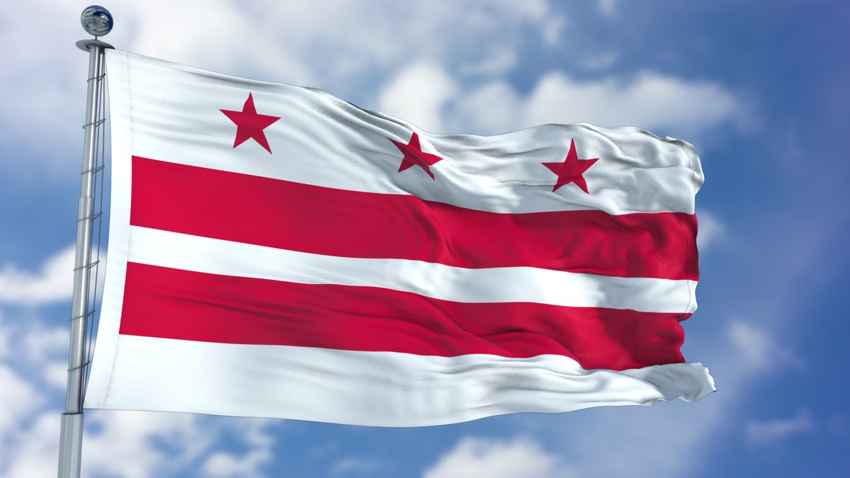 The flag of Washington DC fluttering in front of a blue sky and clouds.