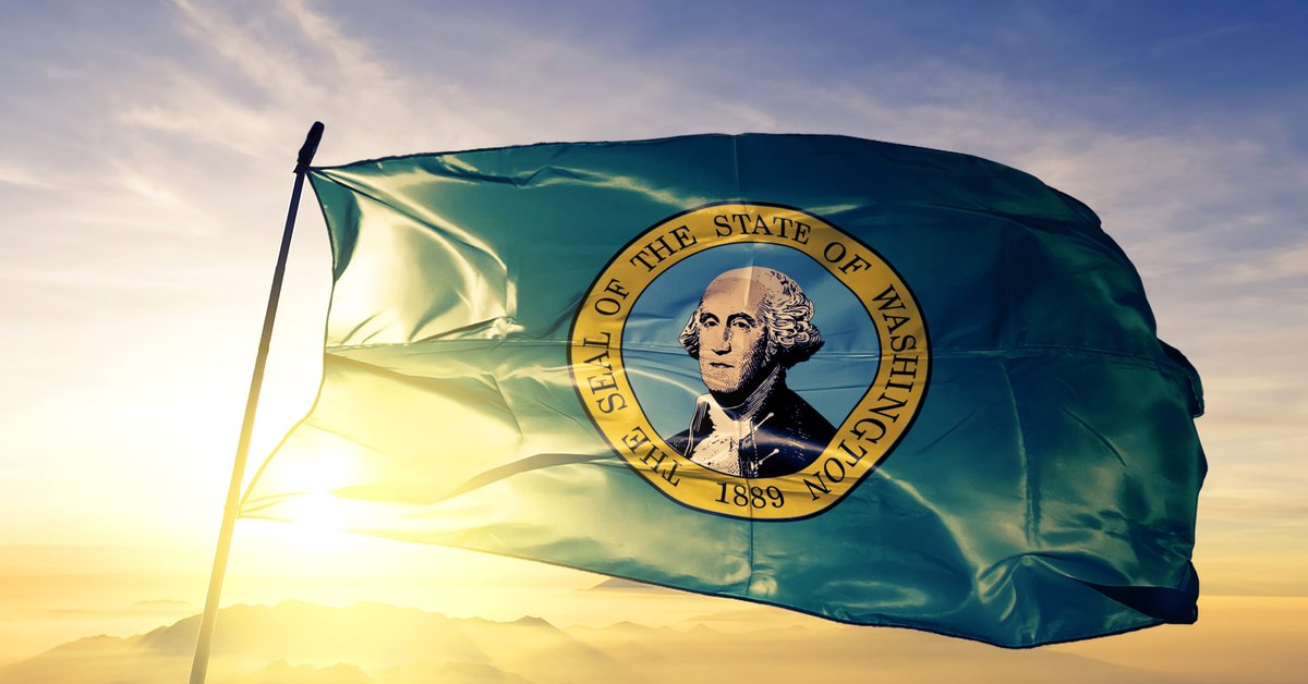 The state flag of Washington flying in front of a sunny sky.